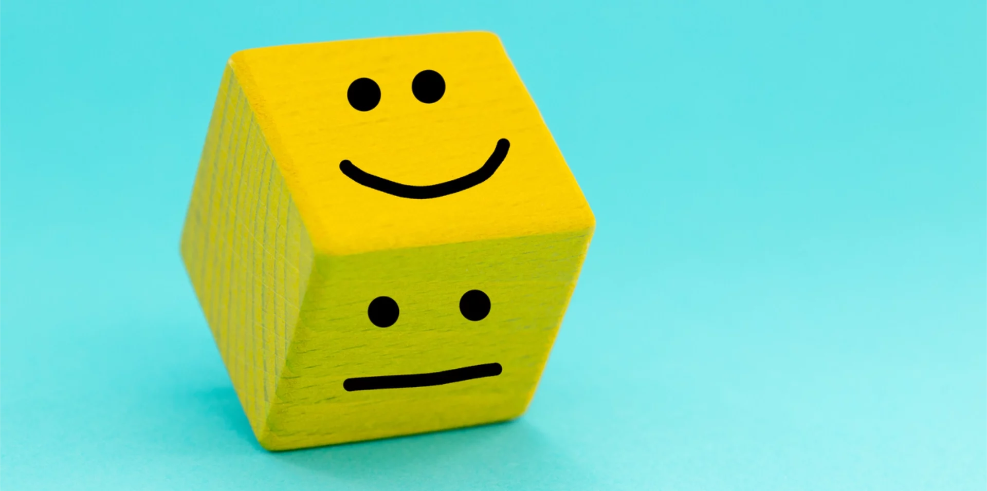 Yellow wooden dice with smiley face and straight face drawn on