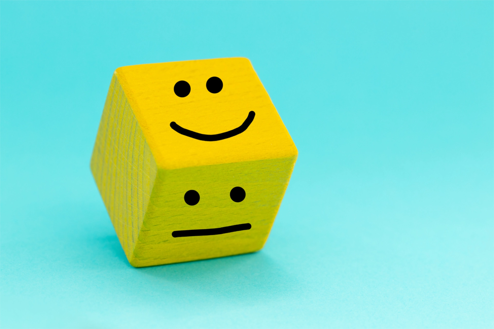Yellow wooden dice with smiley face and straight face drawn on