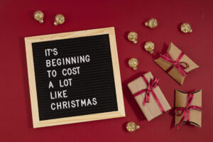 Letter board surrounded by presents with quote; 'It's beginning to cost a lot like Christmas'