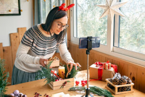 Woman with a phone on a stand arranging Christmas presents for her Christmas campaigns