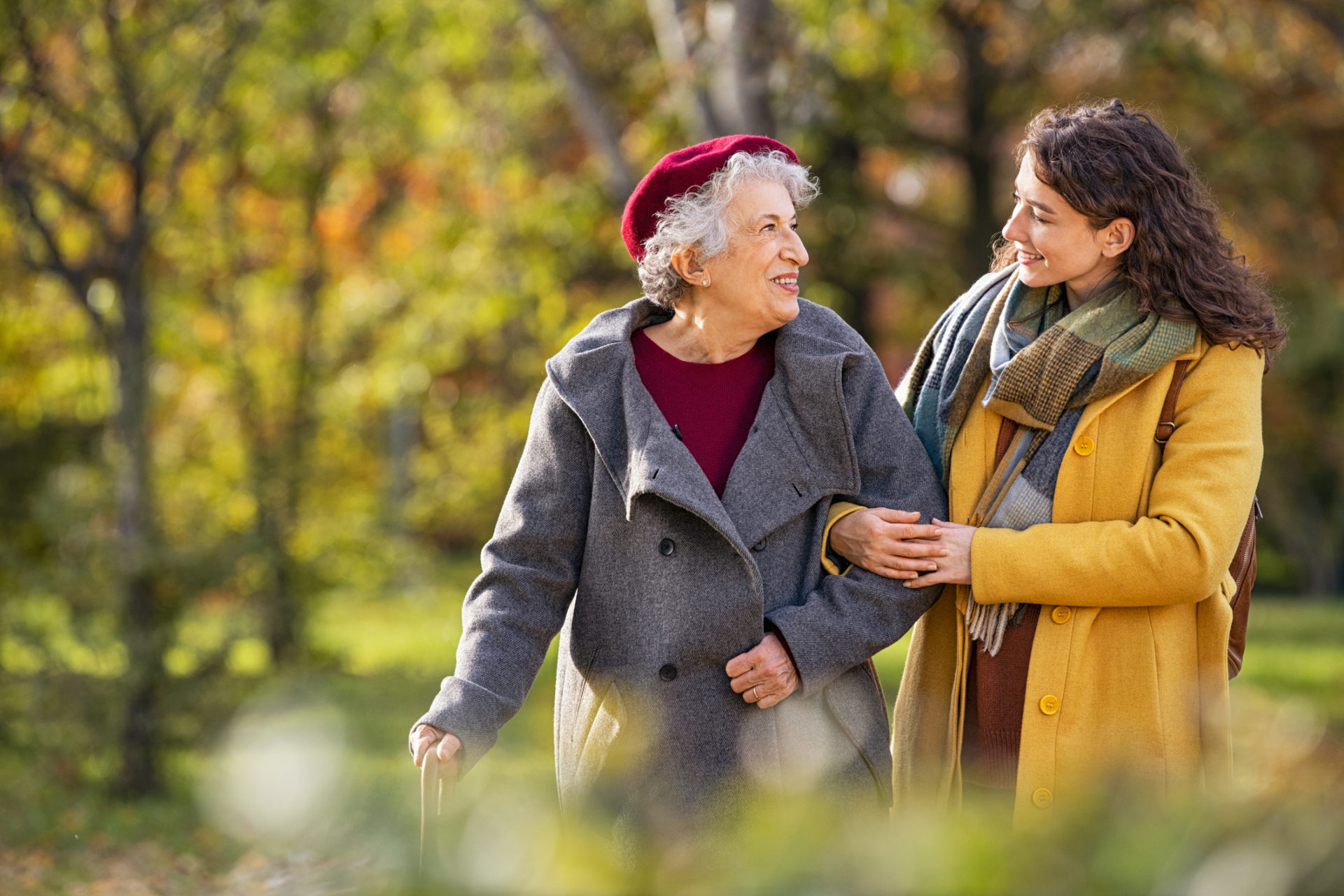 Two women, one older and the other younger, on a walk in nature. They are both looking at each other and smiling.