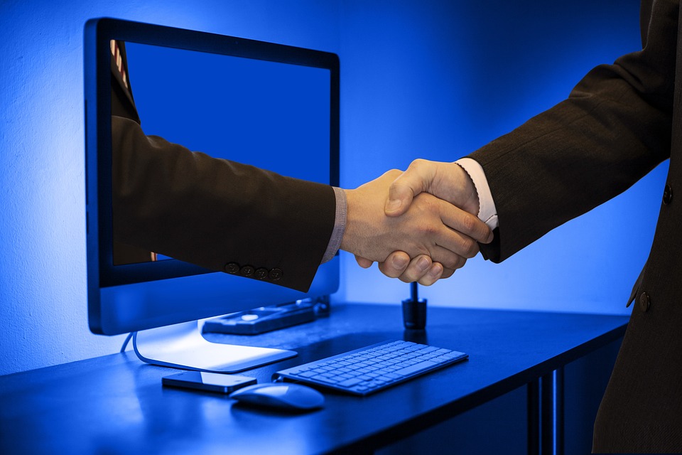 Handshake between two men with one hand coming out of a computer screen