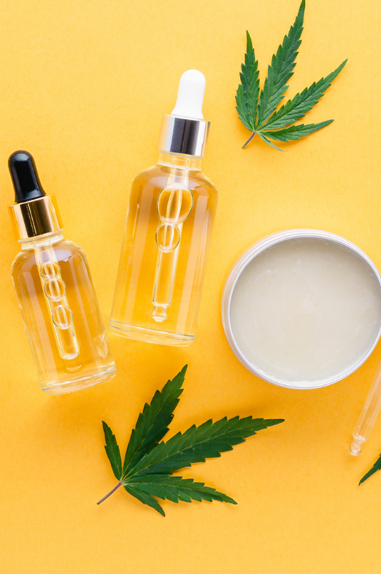 CBD oil and balm with cannabis leaves all on a yellow background